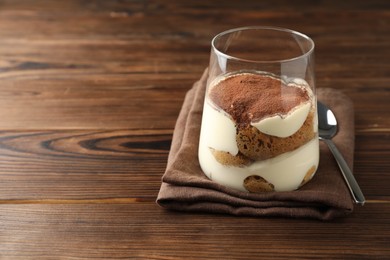 Delicious tiramisu in glass and spoon on wooden table. Space for text