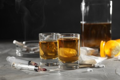 Alcohol and drug addiction. Whiskey in glasses, syringes, pills and cocaine on grey table