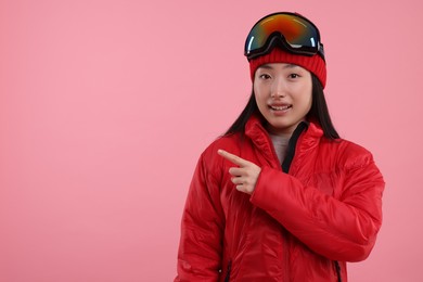 Photo of Happy woman in winter sportswear pointing at something on pink background. Space for text