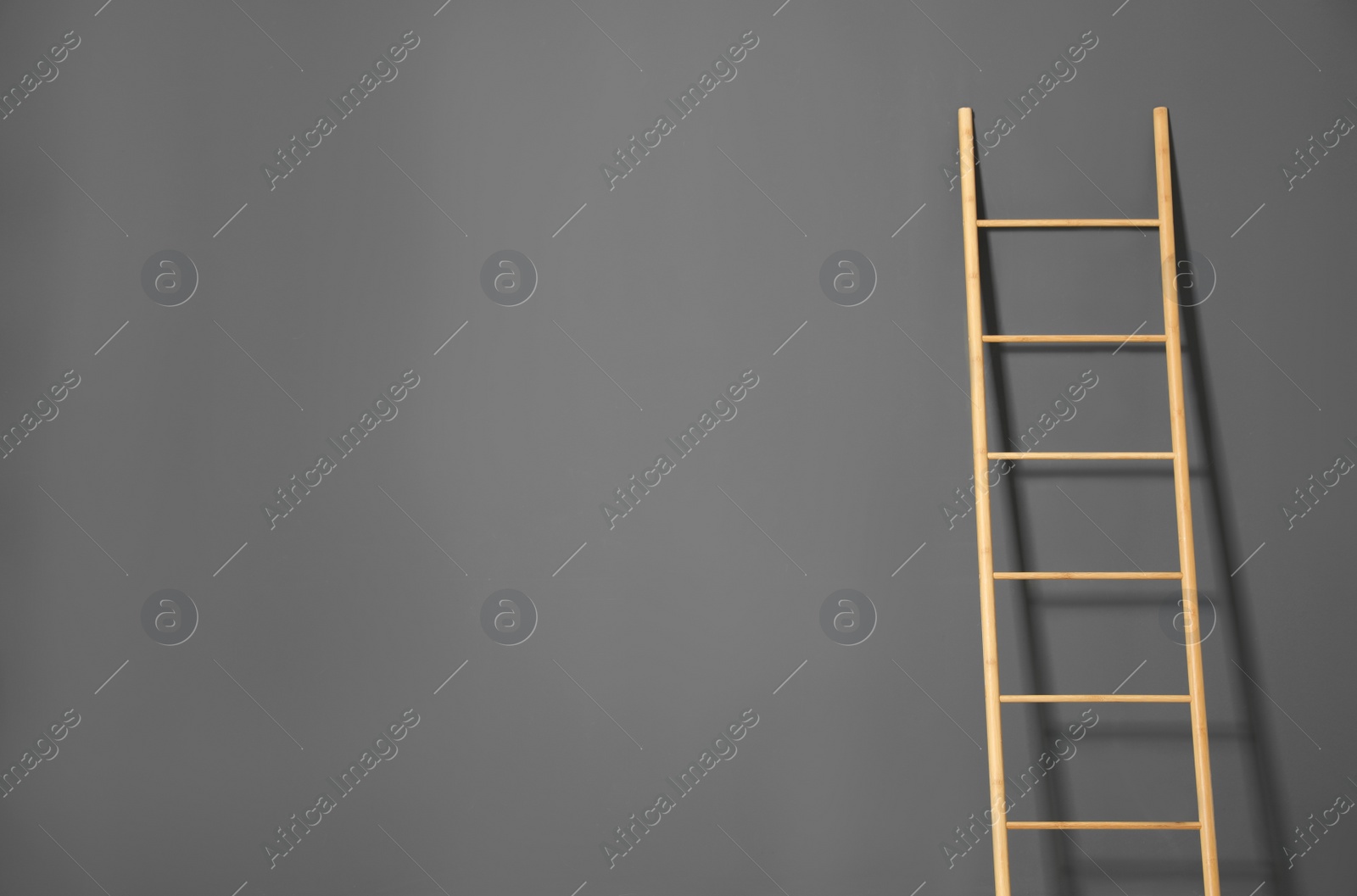 Photo of Modern wooden ladder on grey background. Space for text