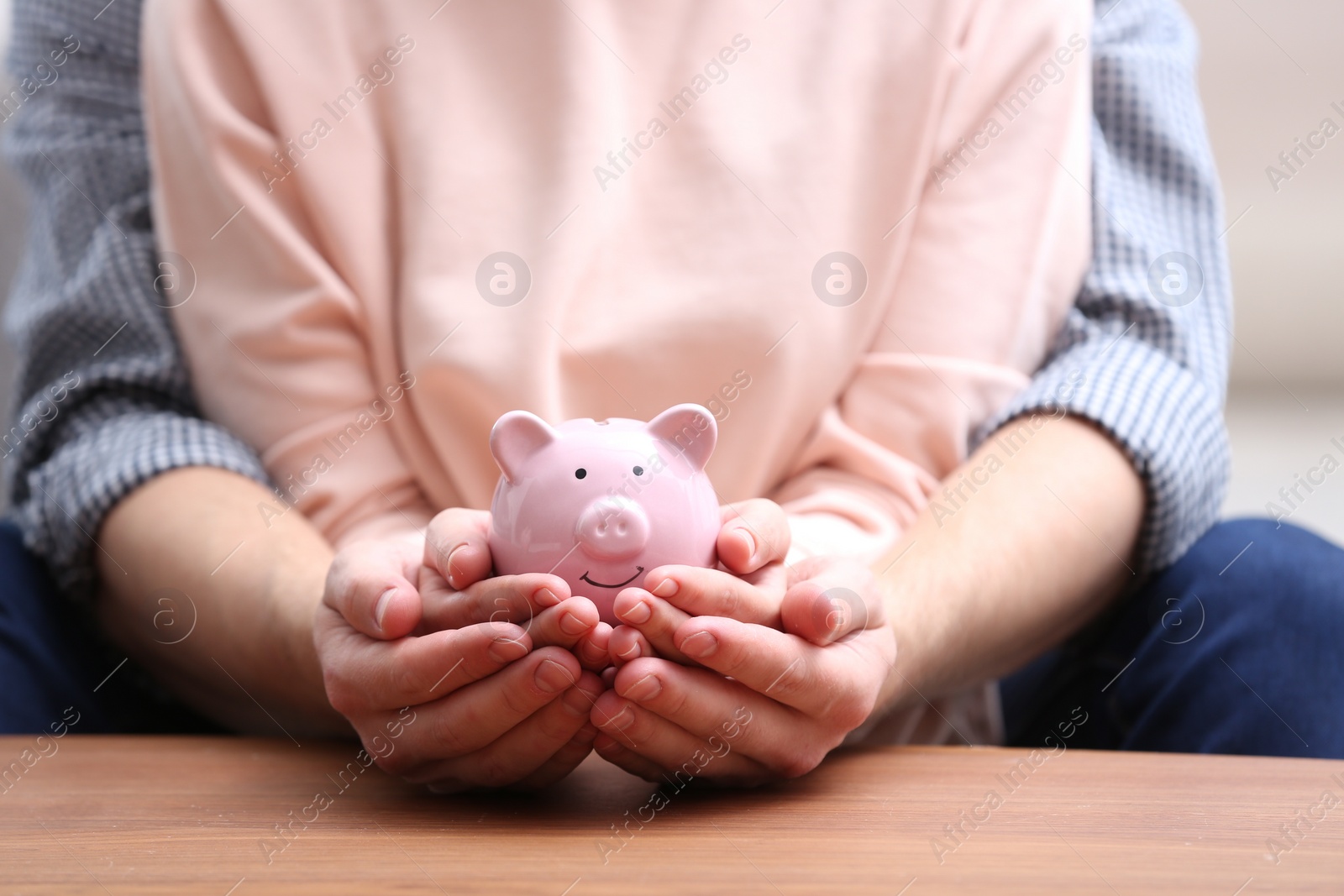 Photo of Couple with piggy bank at wooden table, closeup