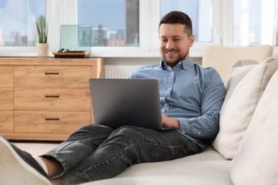 Photo of Happy man working with laptop on sofa at home