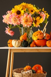 Photo of Autumn composition with beautiful flowers and pumpkins on console table against dark grey background