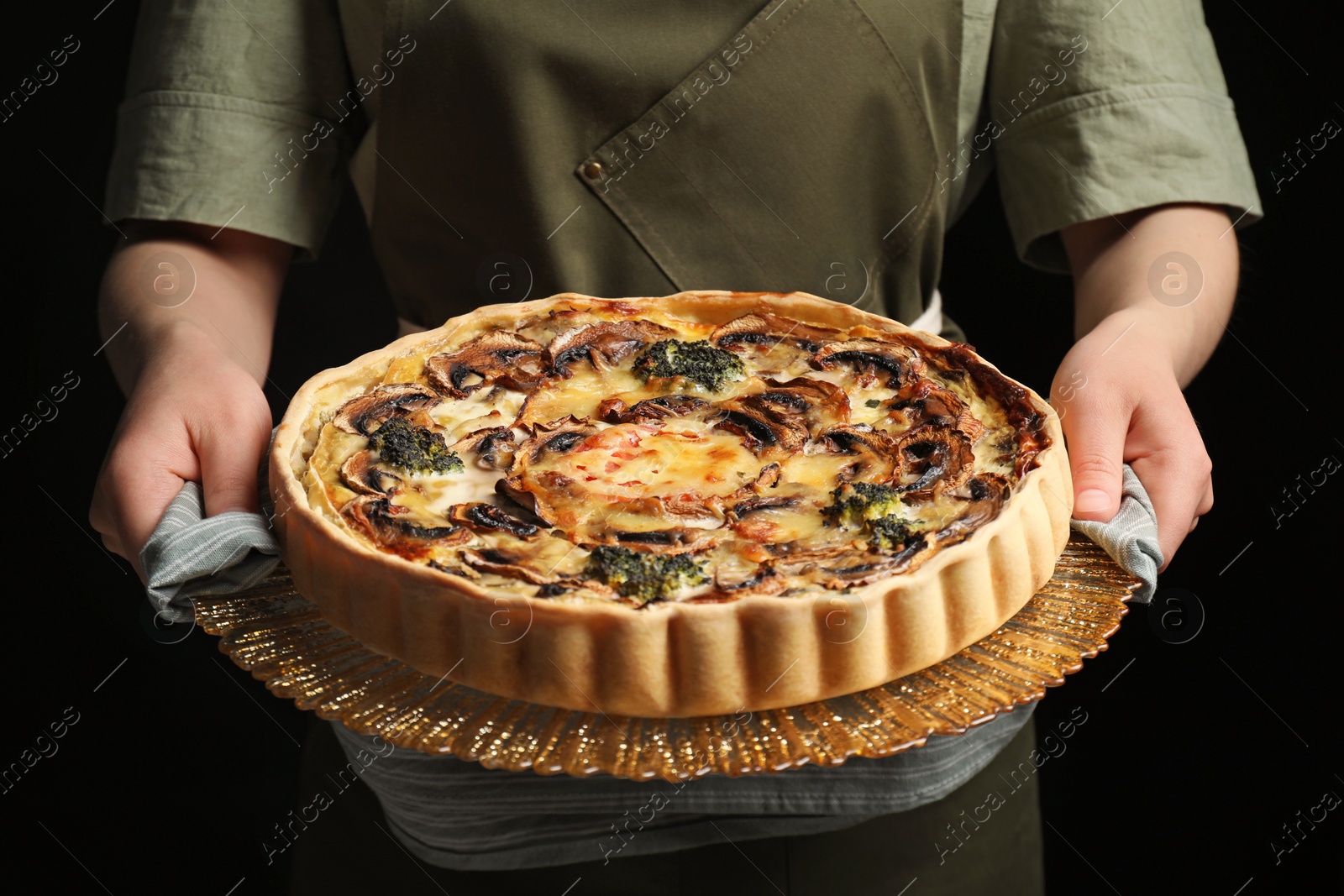Photo of Woman holding delicious homemade quiche with mushrooms against black background, closeup