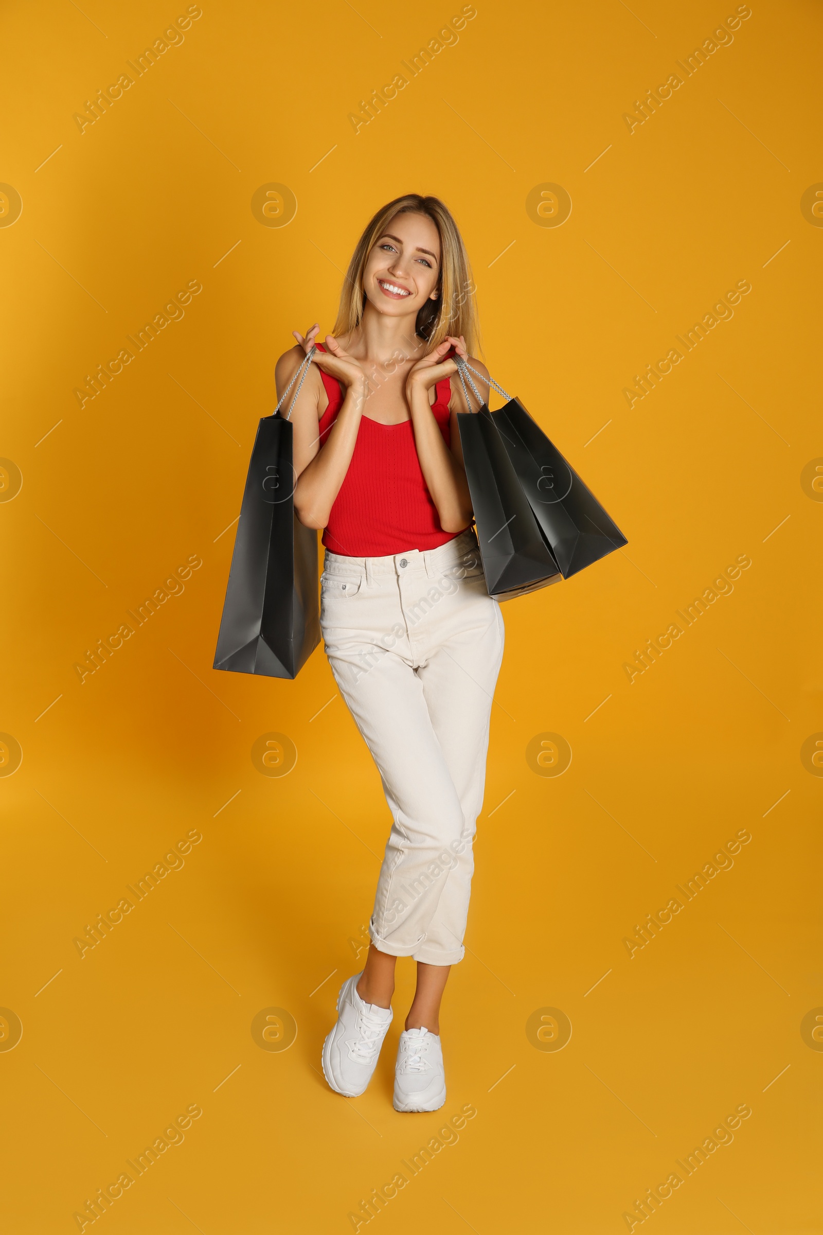 Photo of Happy young woman with shopping bags on yellow background. Black Friday Sale