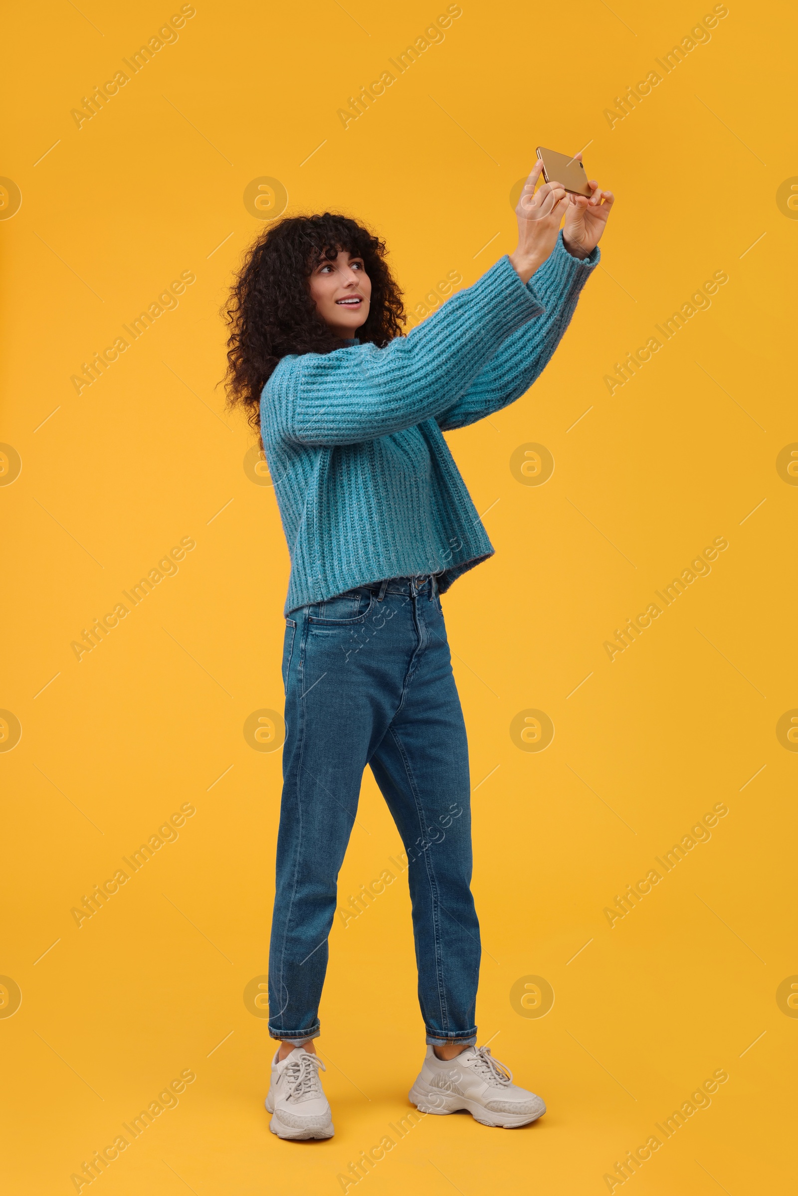 Photo of Beautiful young woman taking selfie with smartphone on orange background