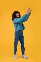 Photo of Beautiful young woman taking selfie with smartphone on orange background