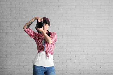 Young female photographer with camera on brick background