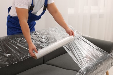 Photo of Worker wrapping sofa in stretch film indoors, closeup