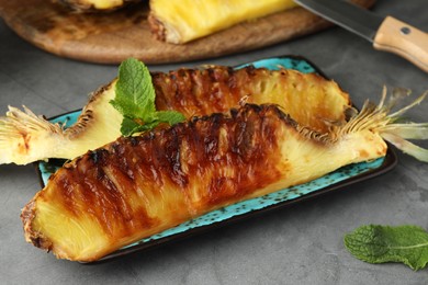 Plate with tasty grilled pineapple pieces and mint leaves on grey textured table, closeup