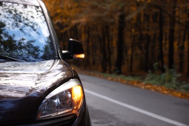 Photo of Modern car on asphalt road near autumn forest, closeup. Space for text