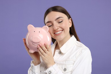 Photo of Happy woman with piggy bank on purple background