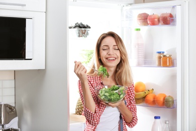 Woman holding bowl with vegetable salad near fridge in kitchen. Healthy diet