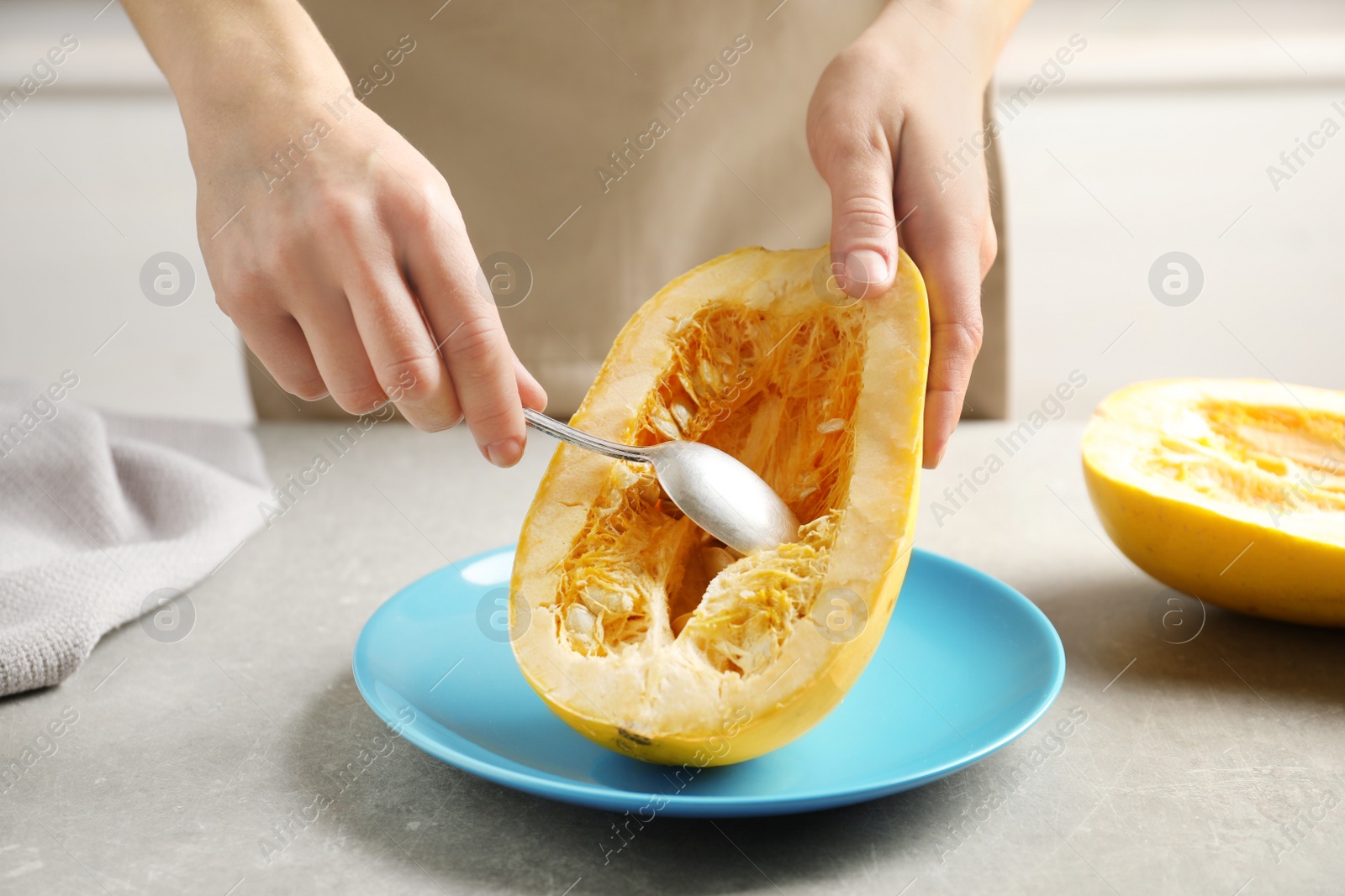 Photo of Woman scraping flesh of spaghetti squash with spoon on table, closeup