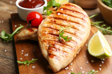Tasty grilled chicken fillet with tomato and lime on wooden board, closeup
