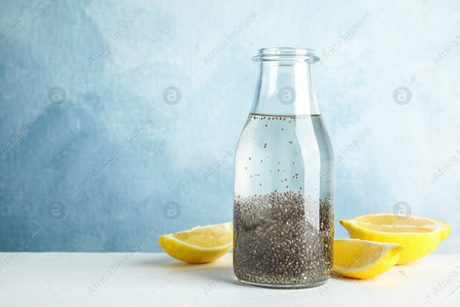 Photo of Bottle of water with chia seeds and lemon on table against color background, space for text