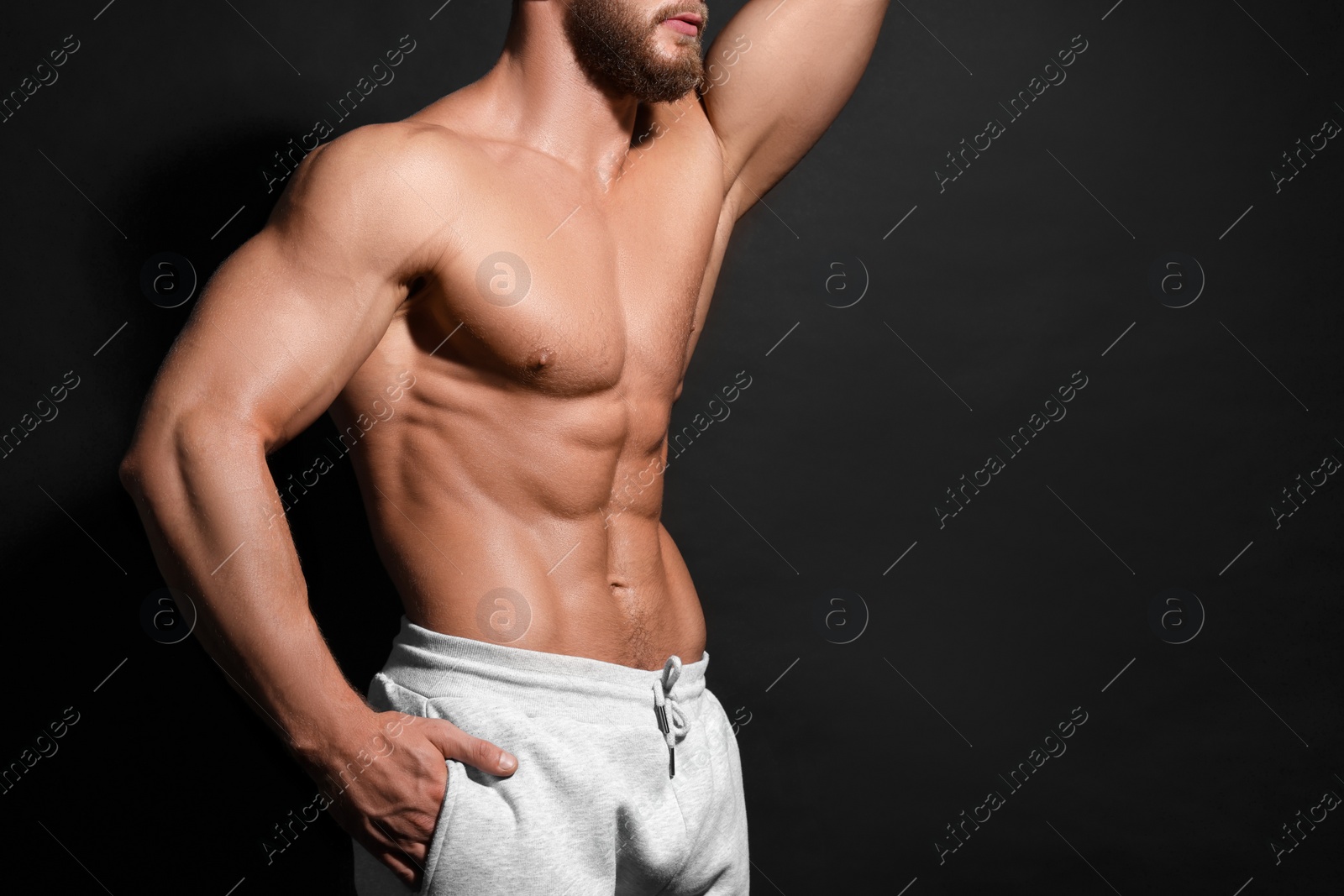 Photo of Muscular man showing abs on black background, closeup and space for text. Sexy body