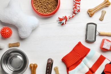 Flat lay composition with dog clothes, food and accessories on white wooden table. Space for text