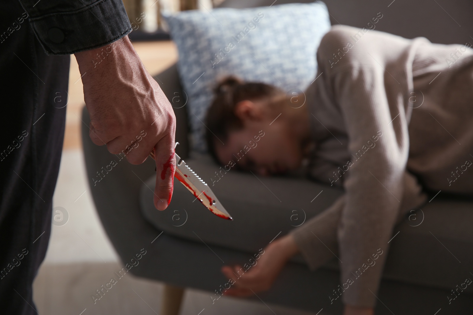 Photo of Man with bloody knife and his victim on couch indoors, closeup. Dangerous criminal