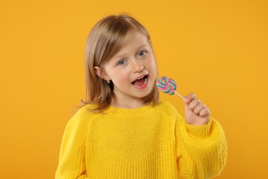 Photo of Portrait of cute little girl with lollipop on orange background