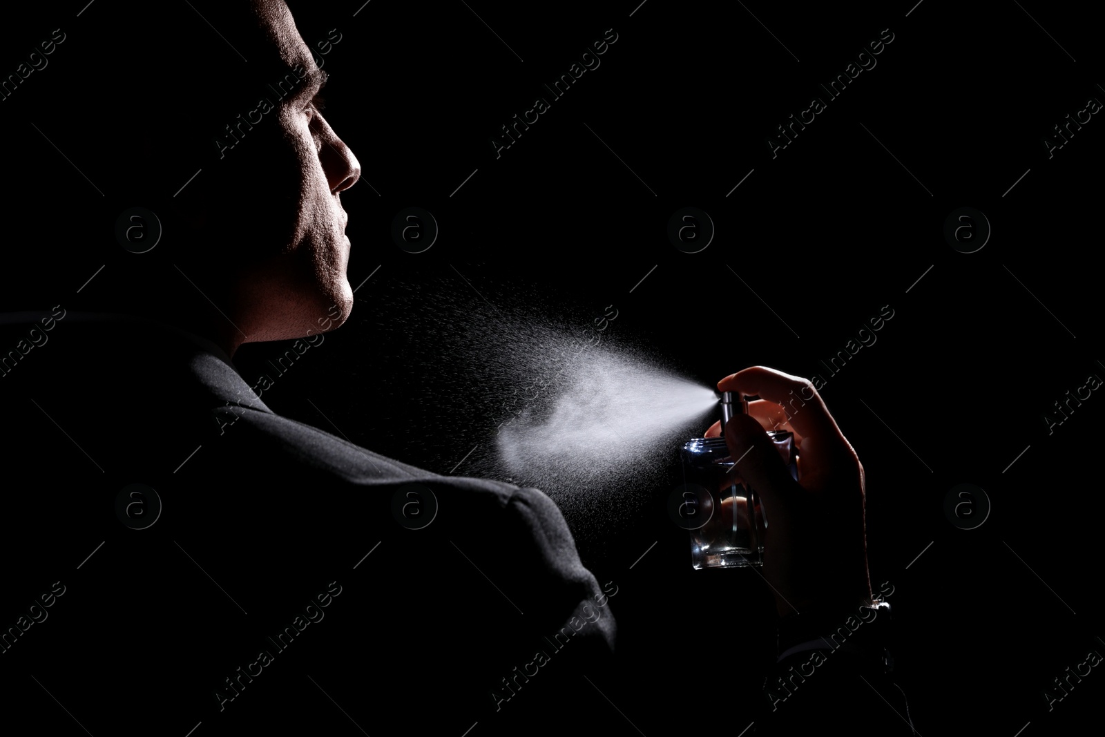 Photo of Man spraying luxury perfume on black background, closeup