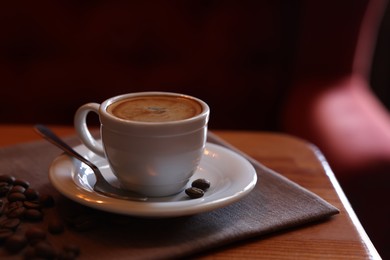 Photo of Cup of hot aromatic coffee and roasted beans on wooden table in cafe. Space for text
