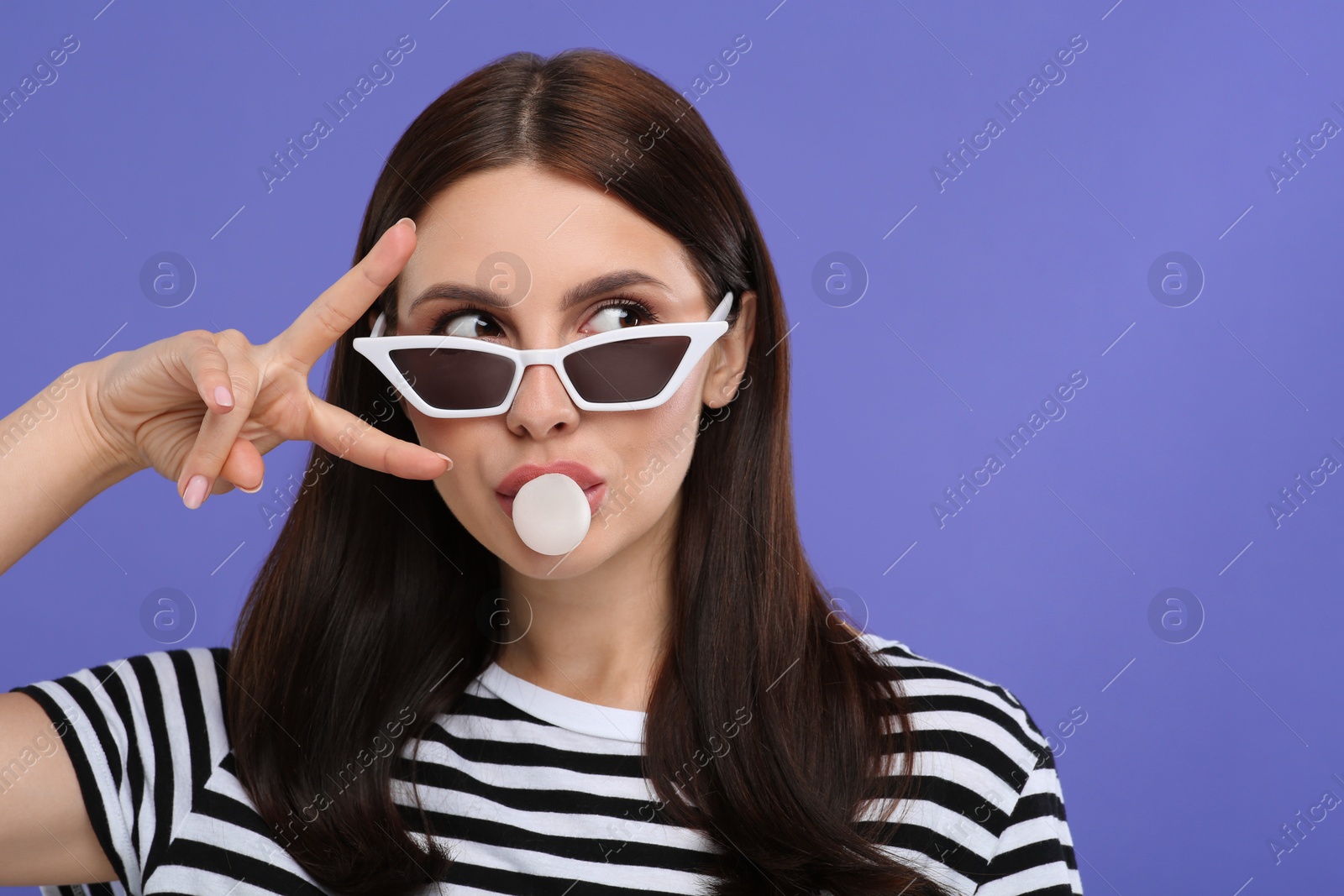 Photo of Beautiful woman in sunglasses blowing bubble gum on light purple background, space for text