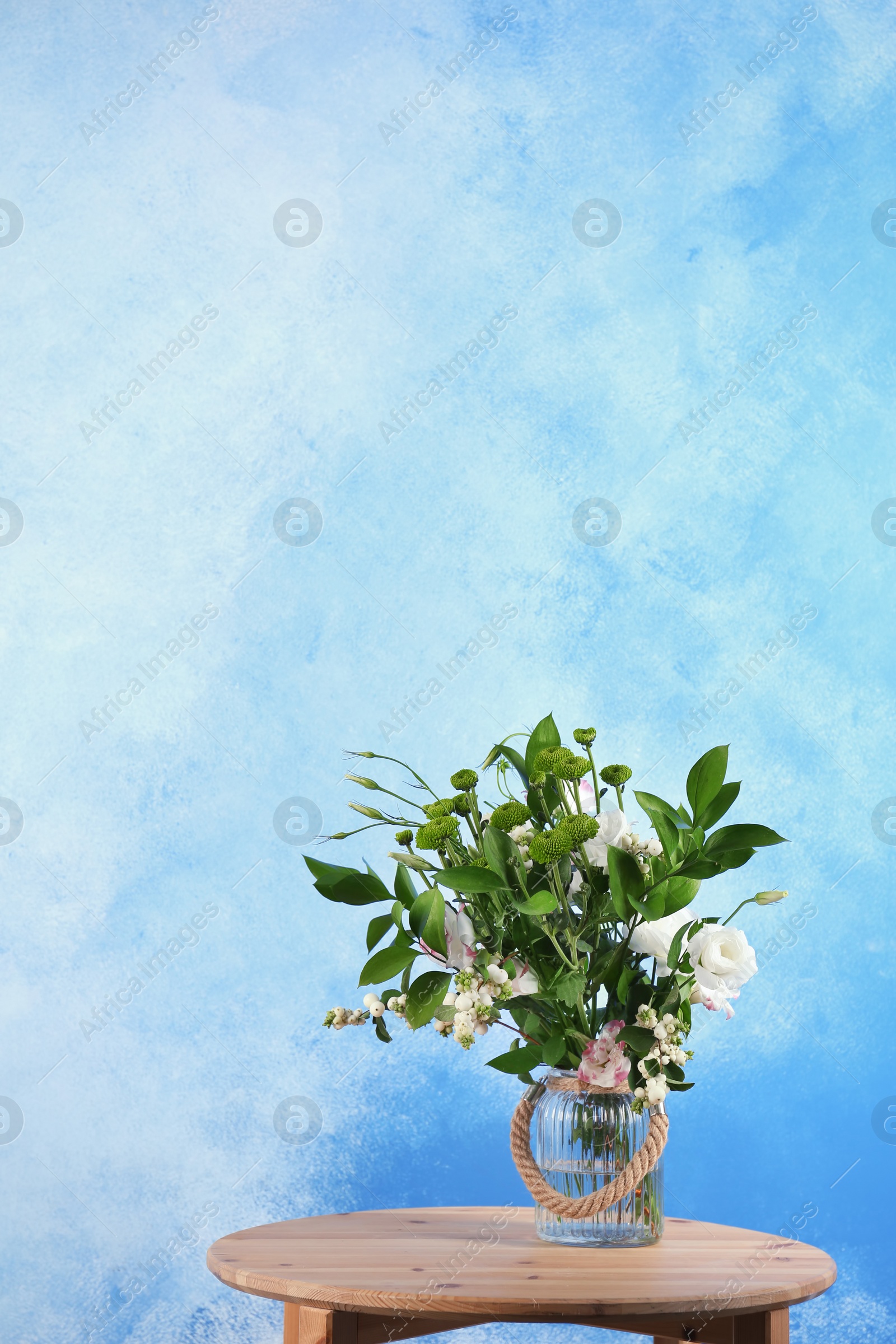 Photo of Vase with bouquet of beautiful flowers on table against color background. Space for text