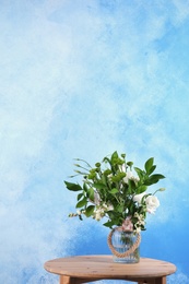 Photo of Vase with bouquet of beautiful flowers on table against color background. Space for text