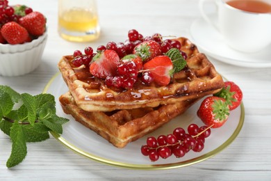 Photo of Plate of delicious Belgian waffles with berries and honey on white wooden table, closeup