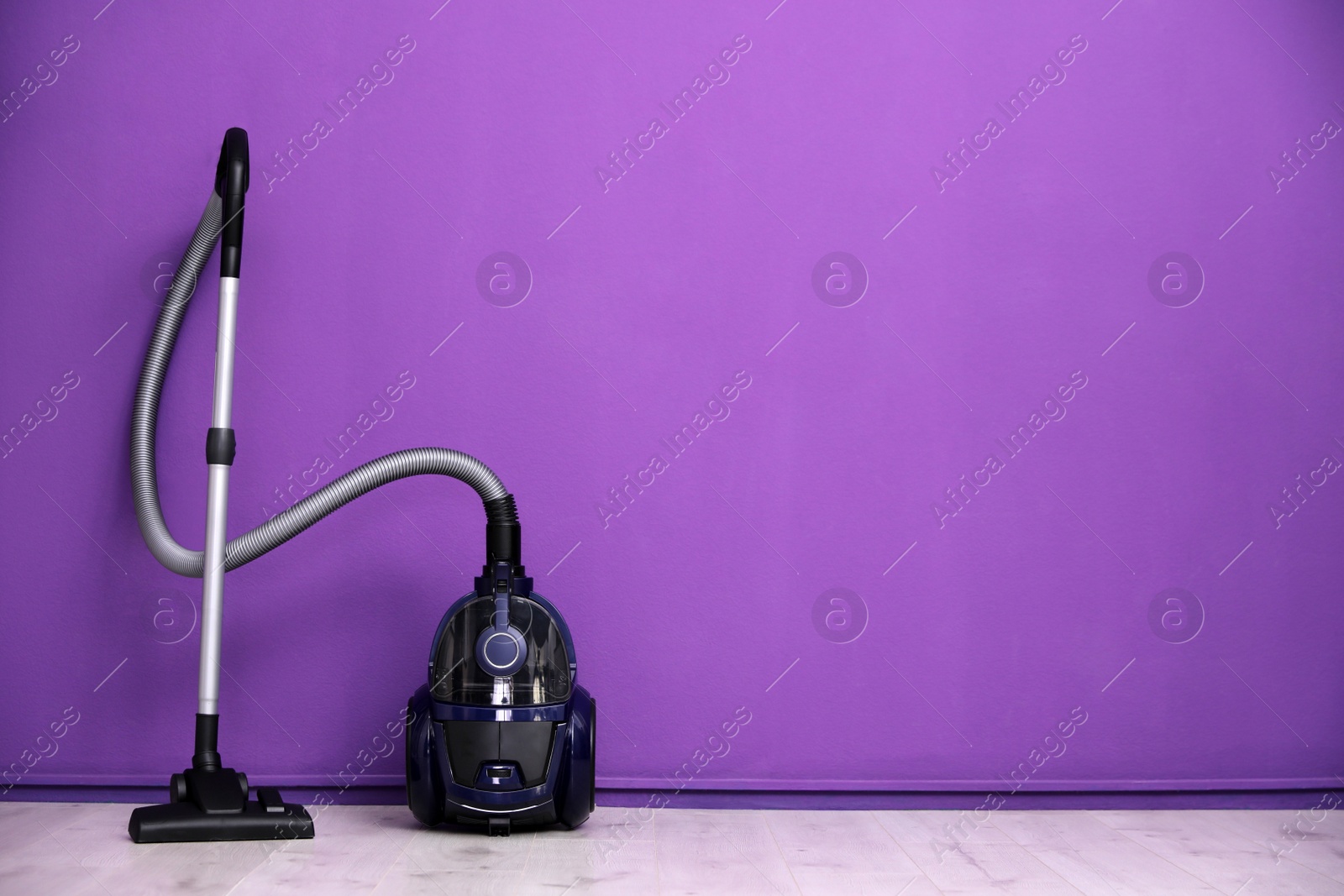 Photo of Modern vacuum cleaner near purple wall indoors, space for text