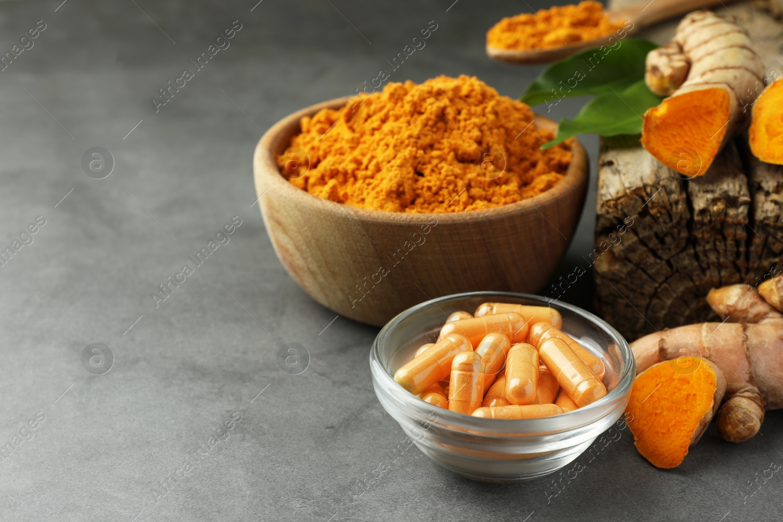 Photo of Aromatic turmeric powder, roots and pills on grey table. Space for text