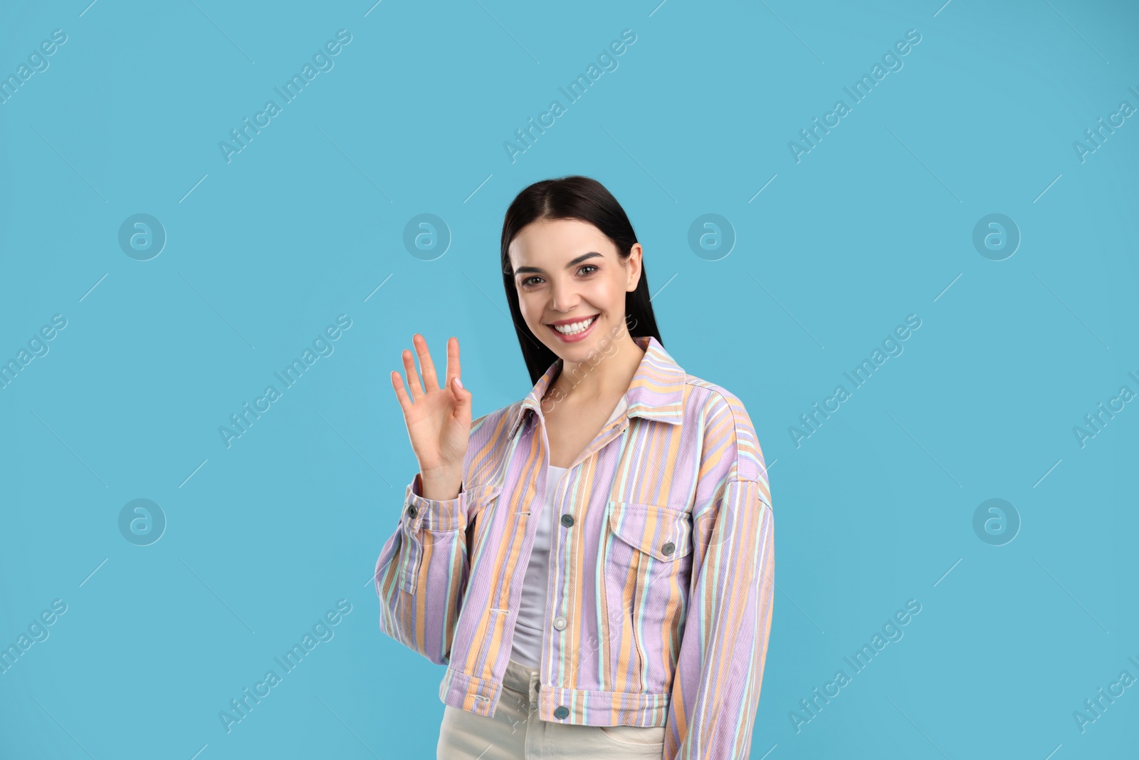 Photo of Attractive young woman showing hello gesture on light blue background