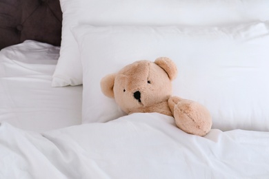 Photo of Cute teddy bear lying in bed indoors. Space for text