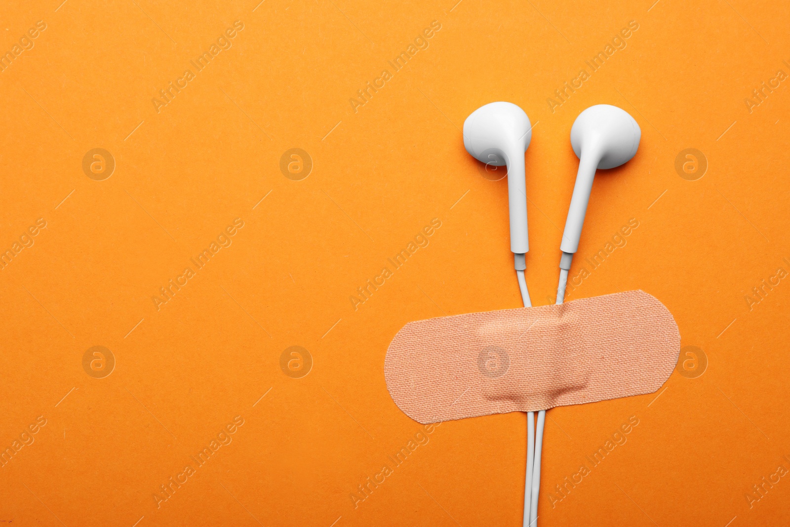 Photo of Wired earphones with sticking plaster on orange background, flat lay. Space for text