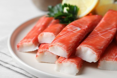 Photo of Plate of fresh crab sticks with lemon on white table, closeup