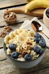 Tasty oatmeal with banana, blueberries and walnuts served in bowl on wooden table