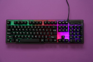 Photo of Modern RGB keyboard on purple background, top view