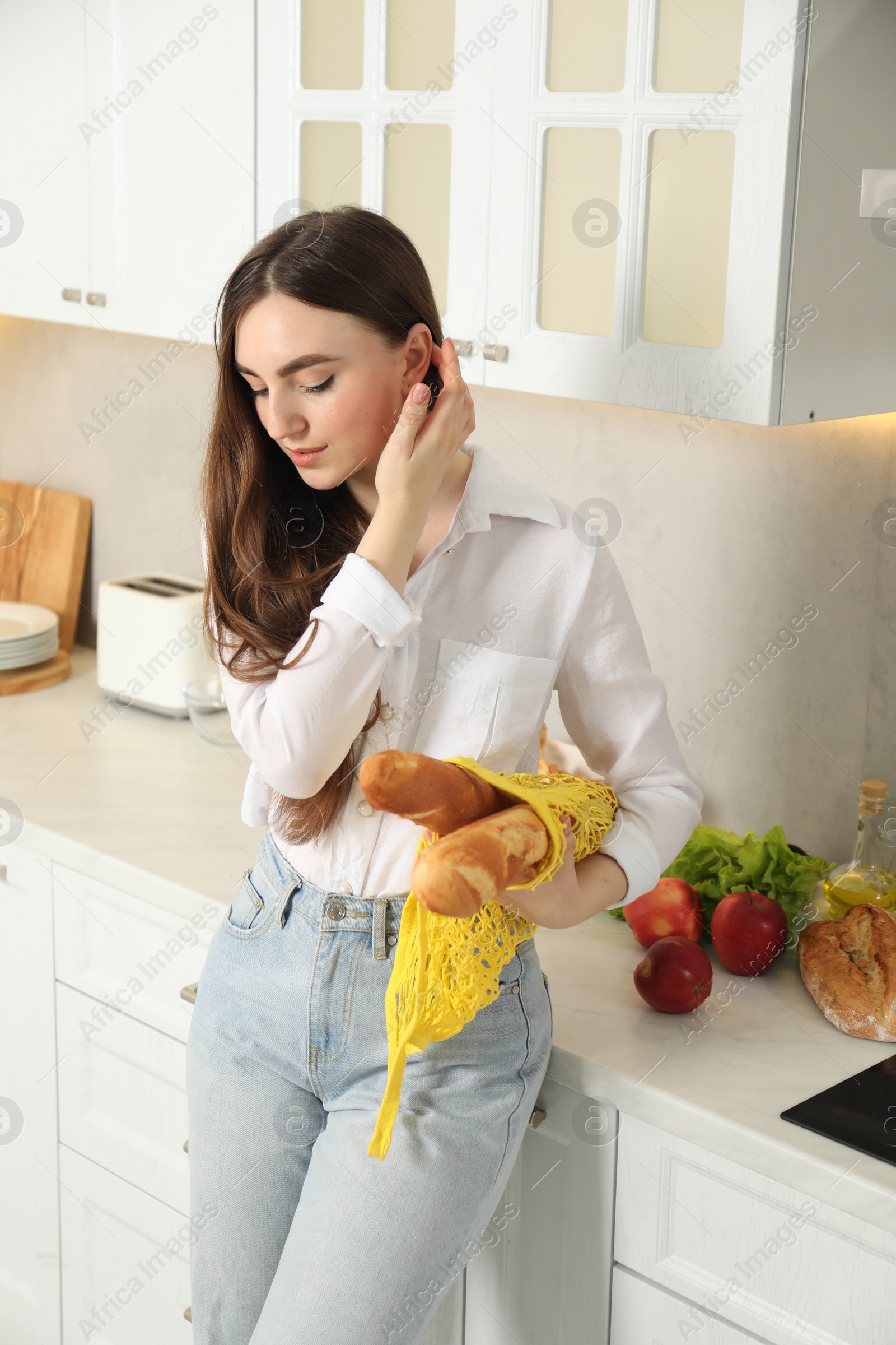 Photo of Woman with string bag of baguettes in kitchen