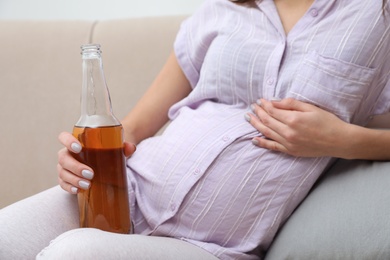 Photo of Future mother with bottle of beer at home, closeup. Alcohol abuse during pregnancy