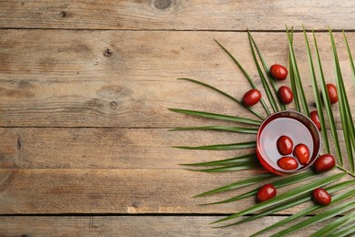 Photo of Palm oil in glass with fruits and tropical leaf on wooden table, flat lay. Space for text