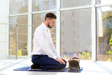 Photo of Muslim man with Koran praying on rug indoors