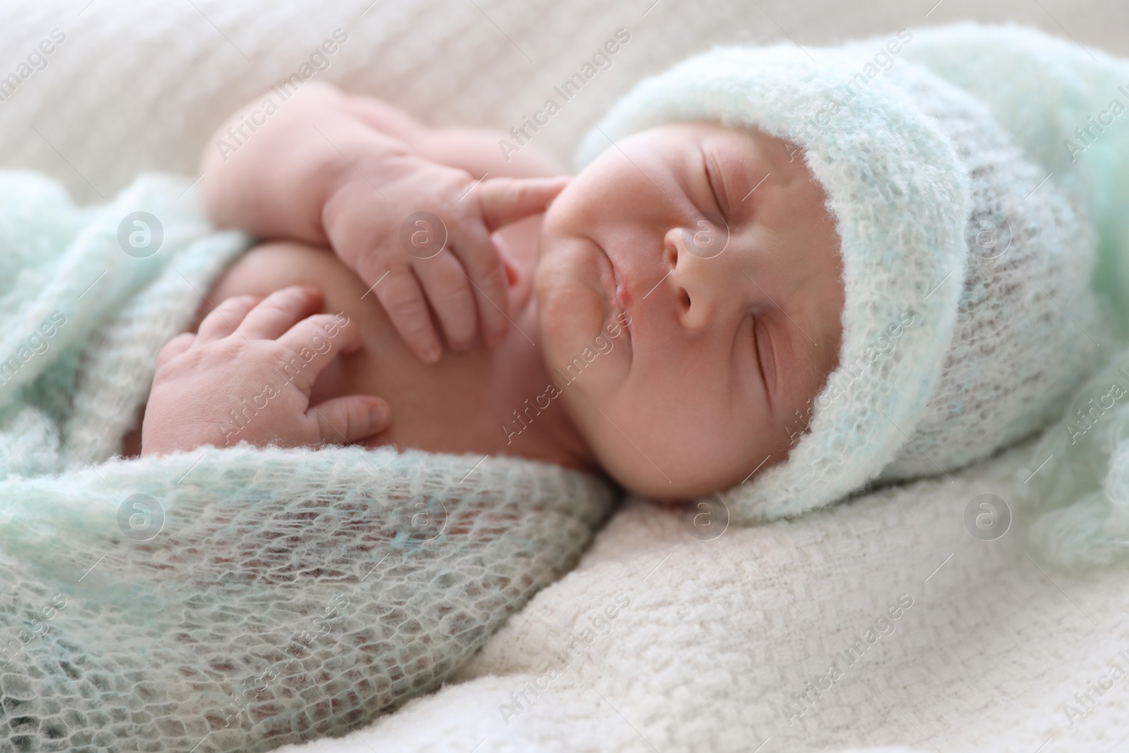 Photo of Cute newborn baby in warm hat lying on white plaid, closeup