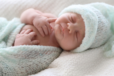 Cute newborn baby in warm hat lying on white plaid, closeup