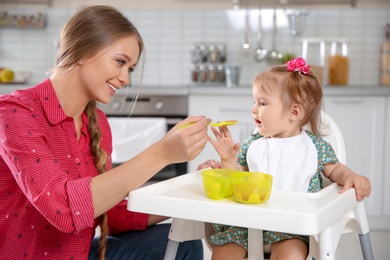 Photo of Mother feeding her little baby with healthy food in kitchen