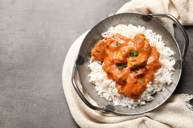 Photo of Delicious butter chicken with rice in dish and napkin on grey background, top view. Space for text