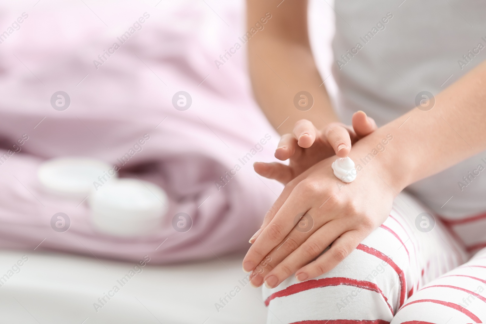 Photo of Young woman applying hand cream on bed at home