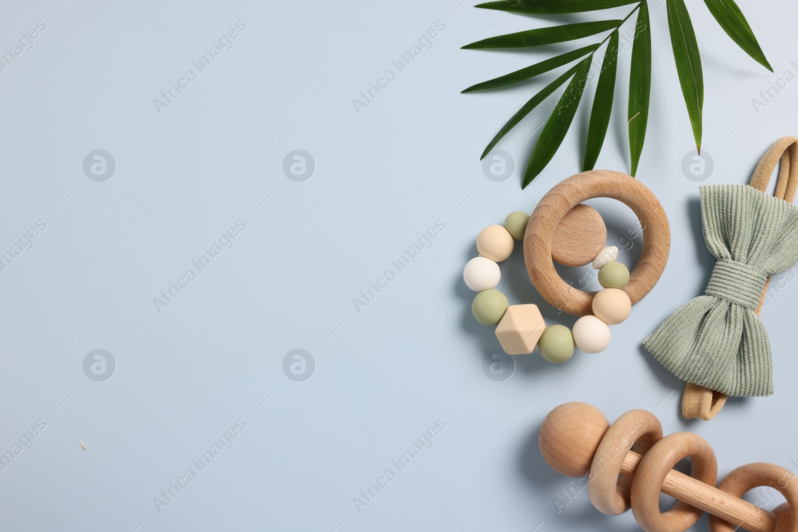 Photo of Baby accessories. Wooden rattles, scrunchy and palm leaf on light blue background, flat lay. Space for text