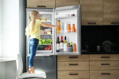 Girl taking bottle with juice out of refrigerator in kitchen