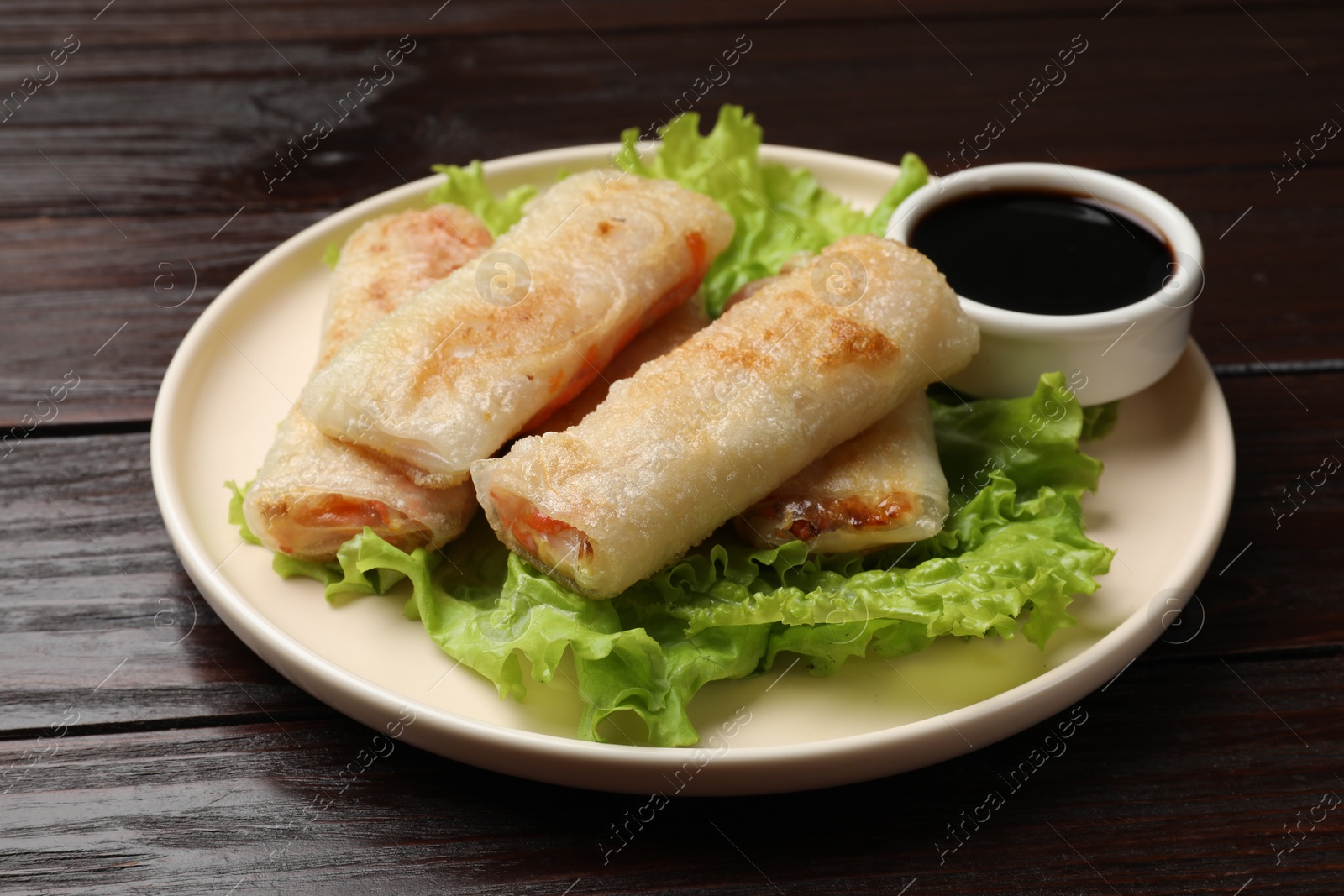 Photo of Delicious fried spring rolls with soy sauce on wooden table, closeup